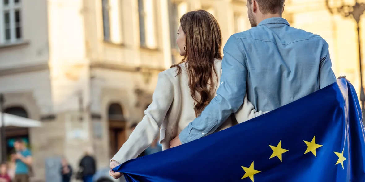 вид сзади молодой пары, завернутой в флаг Европейского Союза, стоящей на улице