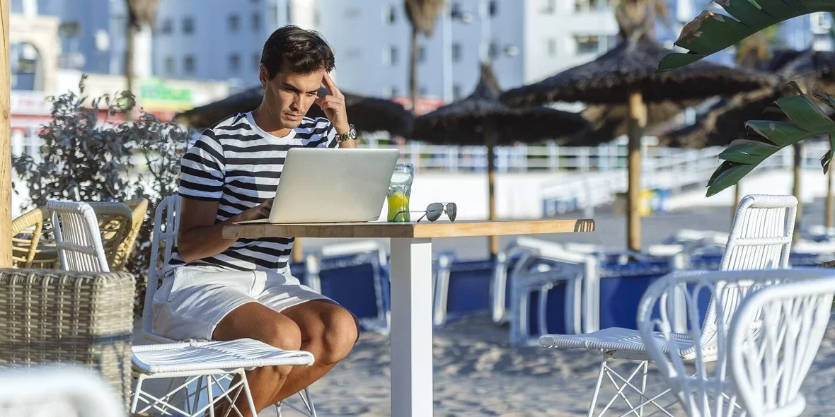 Ein junger Mann sitzt an seinem Laptop vor einem Hintergrund von Palmen