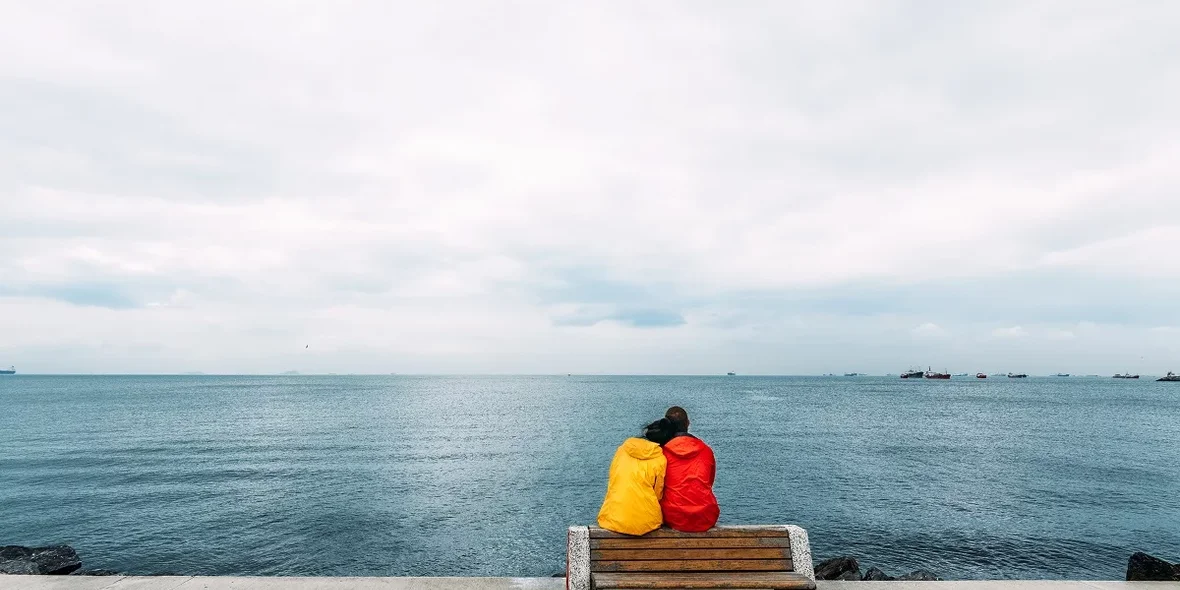 Пара молодых путешественников сидит на скамейке у моря.