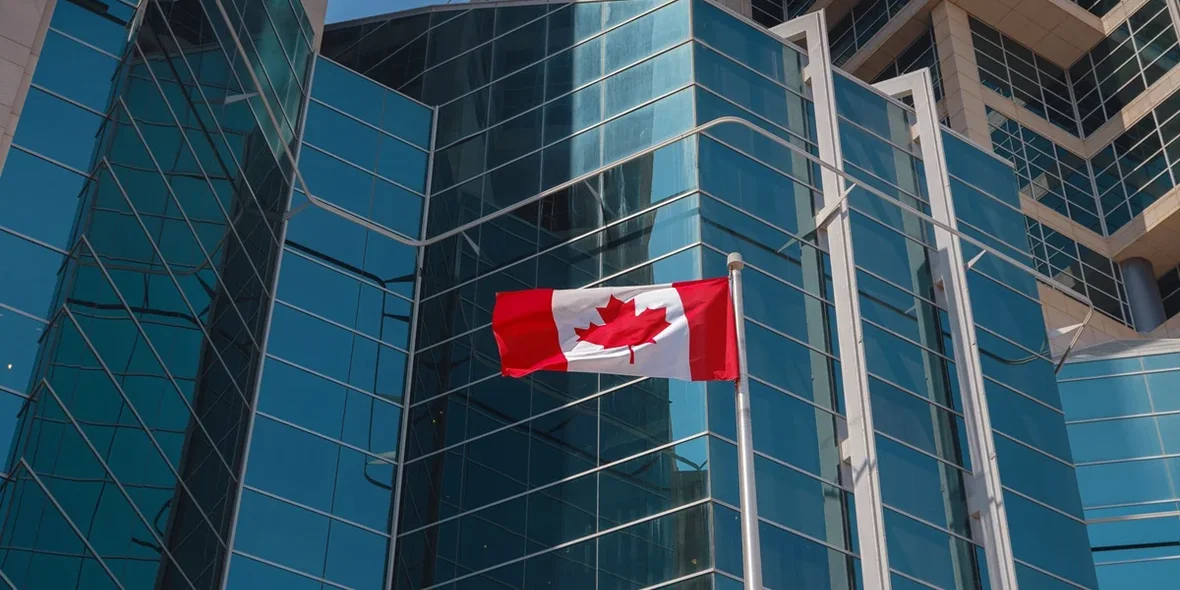 The Canadian flag flying in front of a glass building