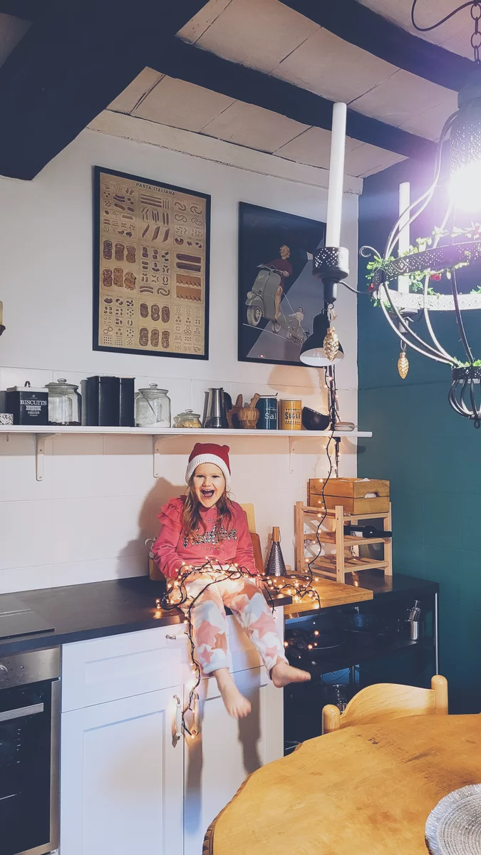 A little girl rejoices as she sits on a table with Christmas lights on it