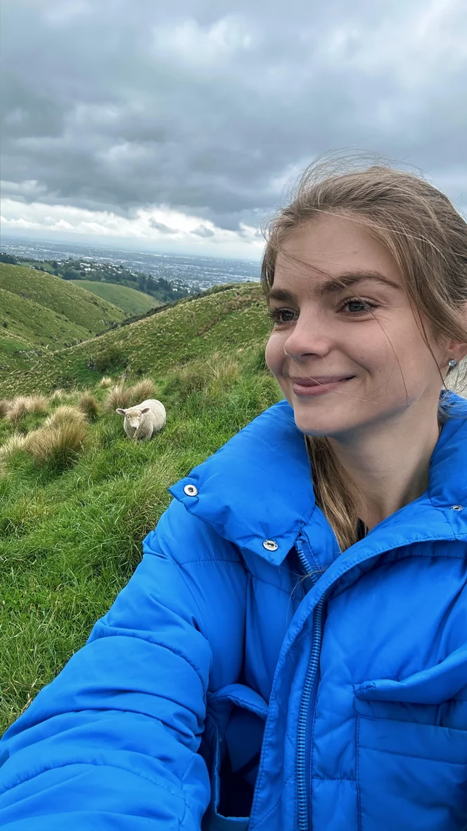 A girl in New Zealand, with a sheep in the background.